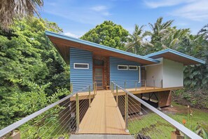 A modern house with a wooden deck and a bridge leading to the entrance. - Tranquil Island Escape at Kehena Beach - Private Home at Black Sands and Volcano (Pahoa)