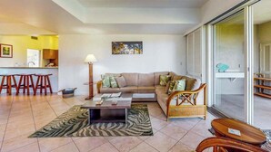 Un salon comprenant un canapé, une table basse et des fauteuils, un coin cuisine et une porte-fenêtre coulissante donnant sur un balcon.