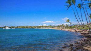 Une plage avec une eau d’un bleu limpide, des palmiers et une côte lointaine parsemée de bâtiments.