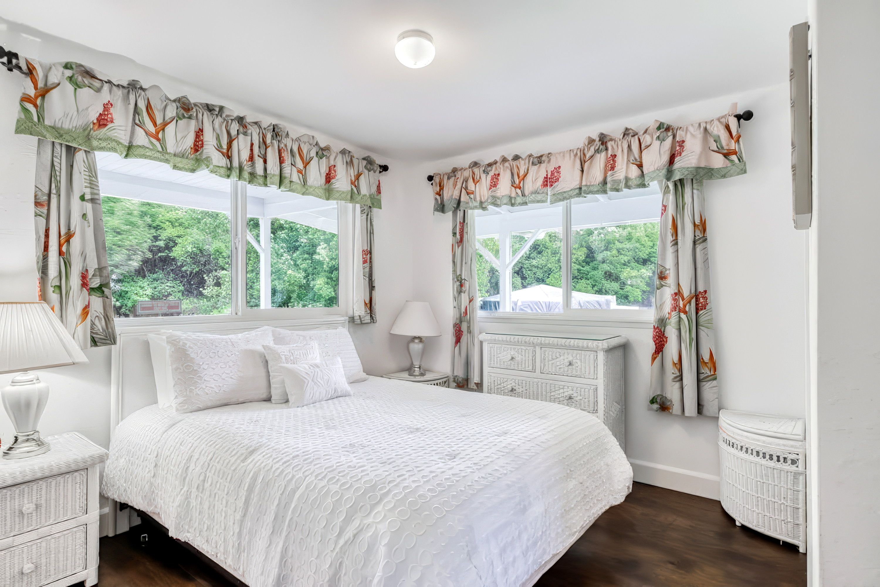 A bedroom with a large bed, two bedside tables, a lamp, and curtains with a floral pattern.