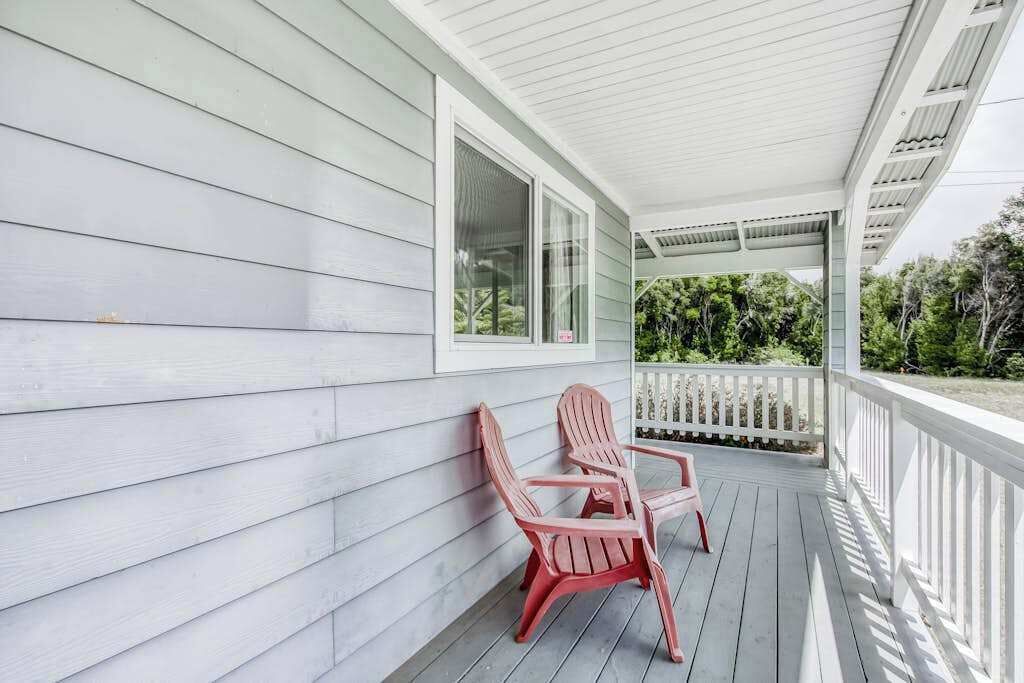 A covered porch with two Adirondack chairs, a white railing, and a view of greenery.