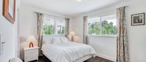 Ein Schlafzimmer mit einem Bett, zwei Nachttischen, einem Fenster mit Vorhängen und einem Bild an der Wand.