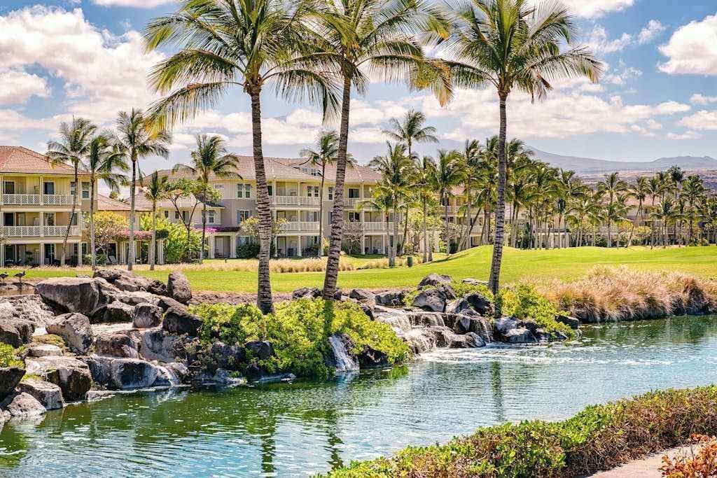 A hotel with a pool, palm trees, and a view of the surrounding landscape.