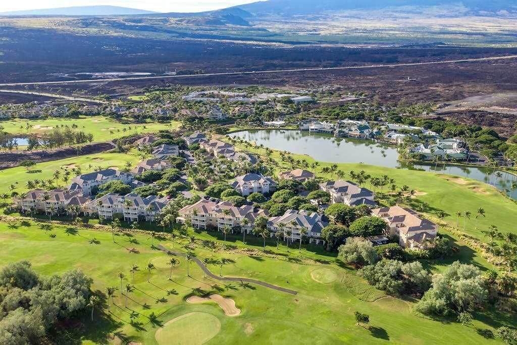 Vue aérienne d’un complexe hôtelier avec un terrain de golf, comprenant plusieurs bâtiments, un lac et de vastes espaces verts bien entretenus.