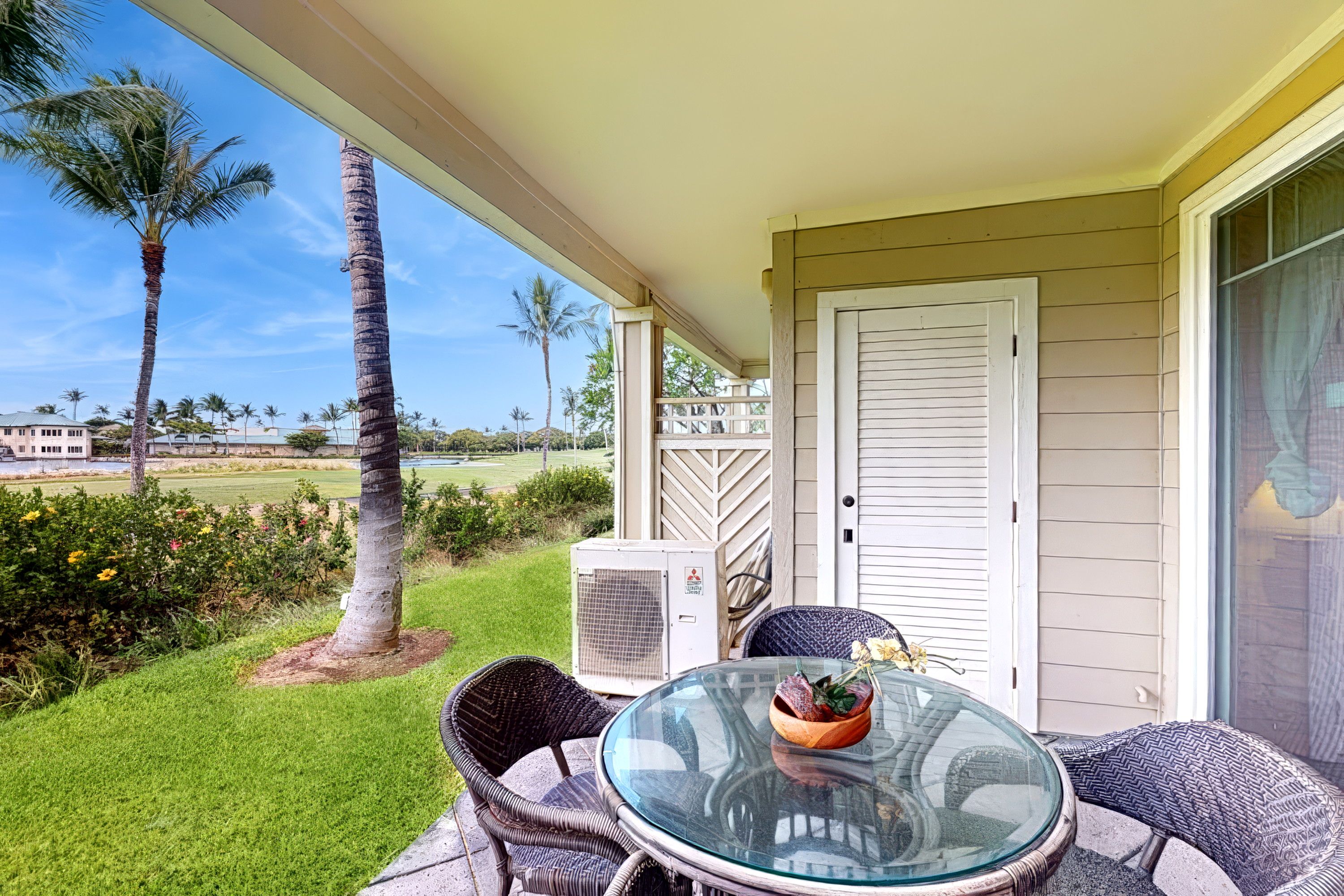 An outdoor patio with a glass table, wicker chairs, and a potted plant.