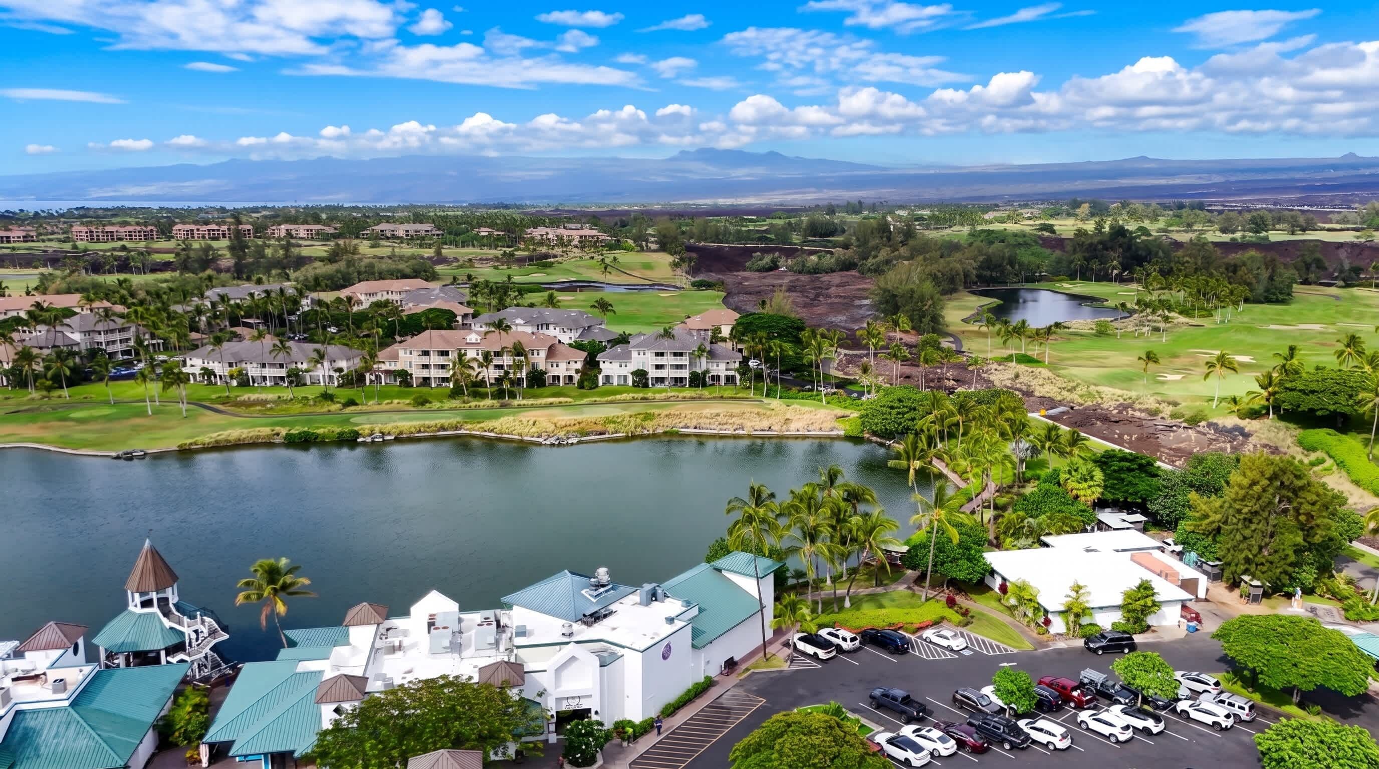 A golf course with a lake, hotel buildings, and a parking lot.