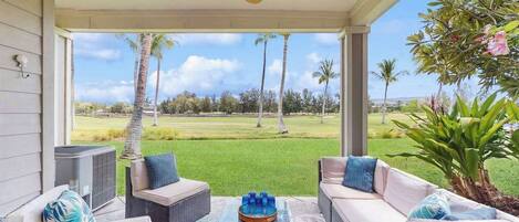 A covered outdoor seating area with wicker furniture, a ceiling fan, and a view of a golf course.