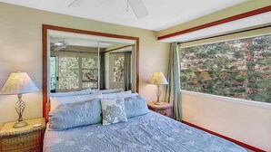 Une chambre à coucher avec un lit, deux tables de chevet, un grand miroir et une fenêtre donnant sur des arbres.