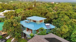 A two-story house surrounded by dense tropical vegetation.