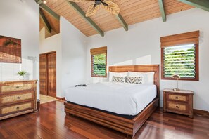 A bedroom with a wooden bed, a ceiling fan, and two windows with blinds.