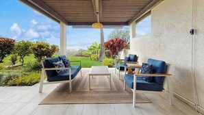 A covered outdoor seating area with a view of a landscaped garden. - *NEW* Kona Sunsets from a Ground Floor Ocean View Lanai (Kailua-Kona)