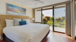 A modern hotel room with a large bed, a ceiling fan, a view through a sliding glass door, and a painting on the wall. - *NEW* Kona Sunsets from a Ground Floor Ocean View Lanai (Kailua-Kona)