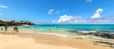 A beach with clear turquoise water, sandy shore, and a few people swimming.