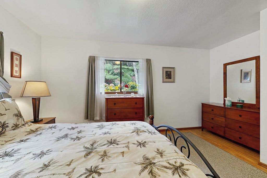 Een slaapkamer met een bed, een kaptafel, een spiegel, een raam met gordijnen en een nachtkastje met een lamp.