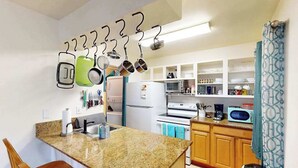 A kitchen with a granite countertop, wooden cabinets, a refrigerator, a microwave, and hanging utensils. - *NEW* Fall $pecial Heated Pool, Hot Tub and Golf in Waikoloa Village (Waikoloa Village)