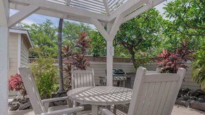 A covered patio area with a white table and chairs, surrounded by various plants and trees. - *NEW* Fall $pecial Heated Pool, Hot Tub and Golf in Waikoloa Village (Waikoloa Village)