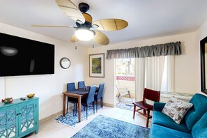 A living room with a ceiling fan, a dining table with chairs, a sofa, a TV mounted on the wall, and a window with curtains. - *NEW* Fall $pecial Heated Pool, Hot Tub and Golf in Waikoloa Village (Waikoloa Village)