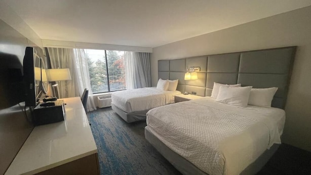 A hotel room with two beds, a desk, a chair, a TV, and a window with curtains.