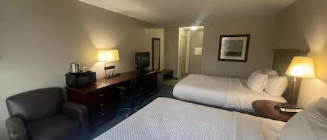 Habitación de hotel con dos camas, un escritorio, una silla y un televisor.