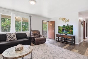 A living room with a leather sofa, a brown recliner, a coffee table, and a television on a wooden stand. - NEW Fall $ale Hamakua Coast Home for Waterfall Days and Family Dinners (Papaikou)