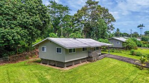 A small, single-story house with a porch, surrounded by lush greenery and trees. - NEW Fall $ale Hamakua Coast Home for Waterfall Days and Family Dinners (Papaikou)