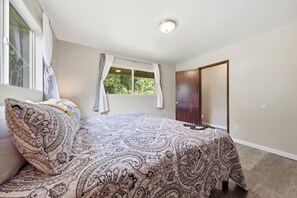 A bedroom with a bed, a window with curtains, a door, and a ceiling light. - NEW Fall $ale Hamakua Coast Home for Waterfall Days and Family Dinners (Papaikou)