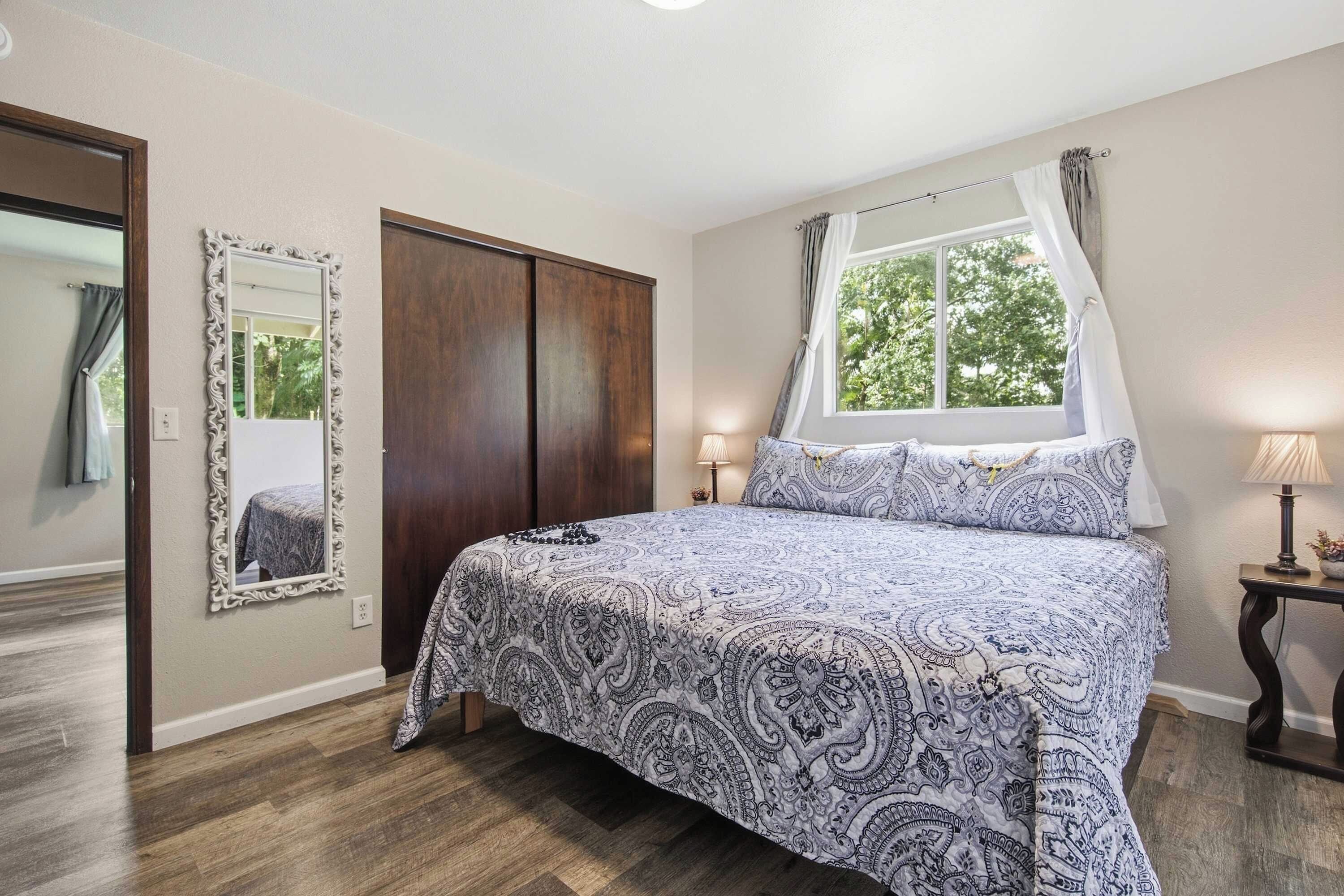Un dormitorio con cama, ventana con cortinas, espejo y puerta.