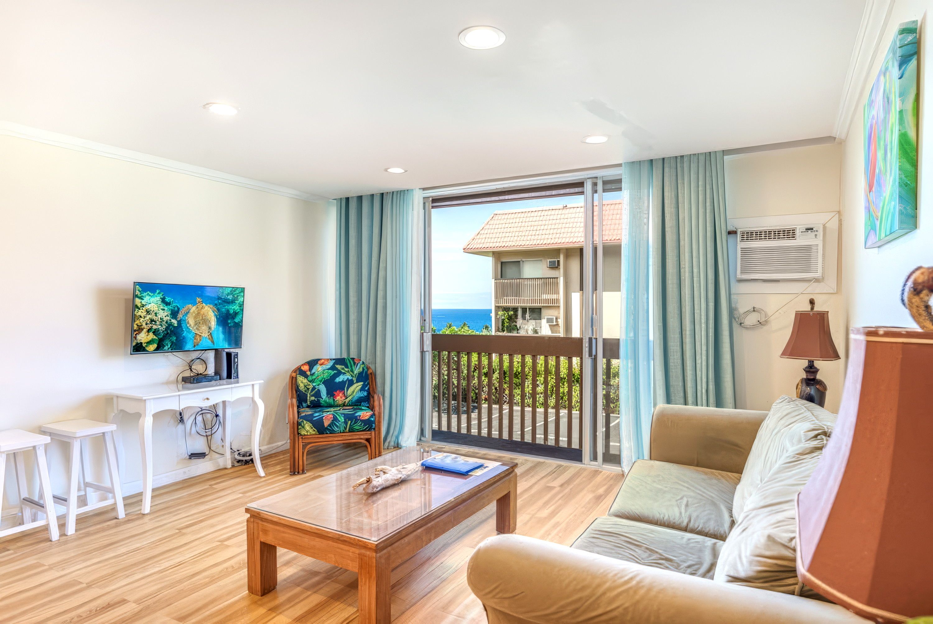Una sala de estar con una mesa de centro de madera, un sofá, una silla, un televisor y un balcón con vista al mar.
