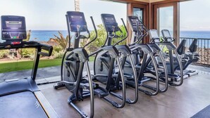 Espaço fitness com esteiras e equipamentos elípticos, com vista panorâmica do oceano.