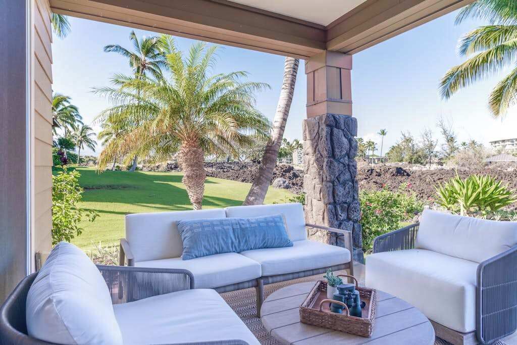 A covered patio with a white sofa, wicker chairs, and a stone pillar.