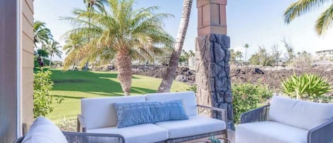 A covered patio with a white sofa, wicker chairs, and a stone pillar.
