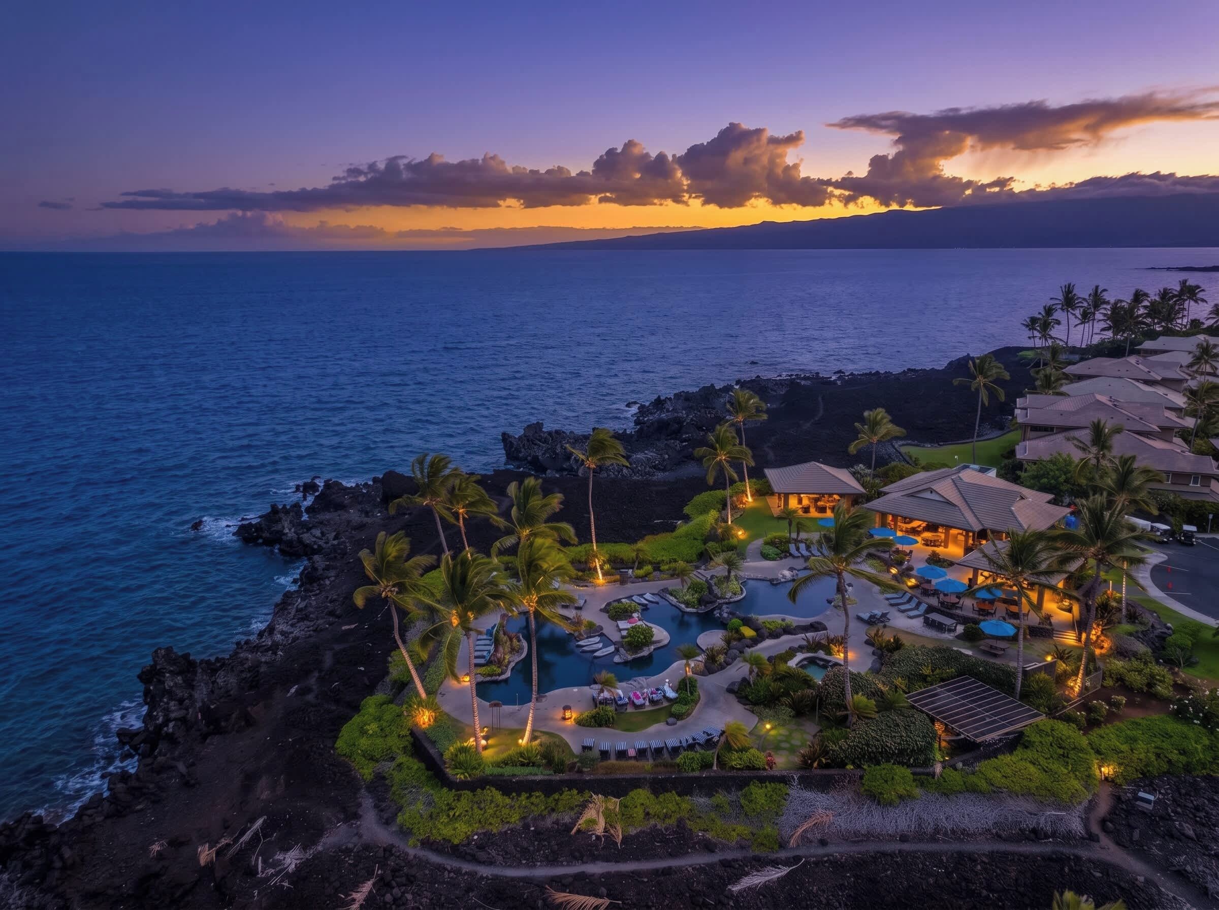A resort with a swimming pool, lounge areas, and a view of the ocean at dusk.