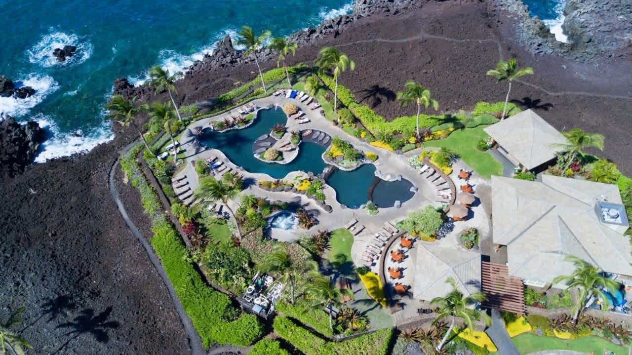 Vue aérienne d’un complexe hôtelier doté de plusieurs piscines, d’une plage et d’un bâtiment au toit en pente.