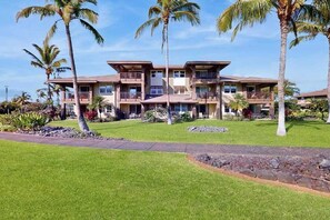 A multi-story hotel with balconies, a well-maintained lawn, and palm trees.