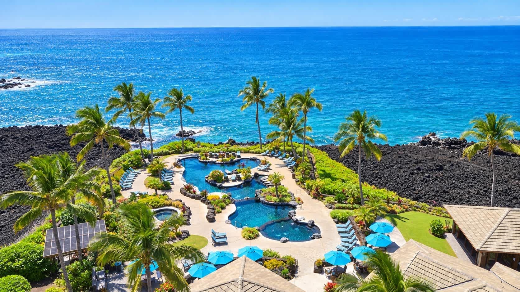 Un resort con múltiples piscinas, palmeras y vista al océano.