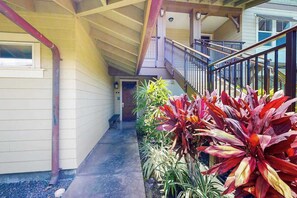 A covered outdoor area with a concrete path, a wooden staircase, and various plants.