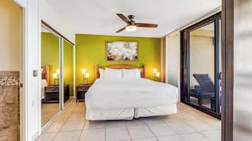 A bedroom with a large bed, a ceiling fan, a painting on the wall, and a sliding glass door leading to a balcony.