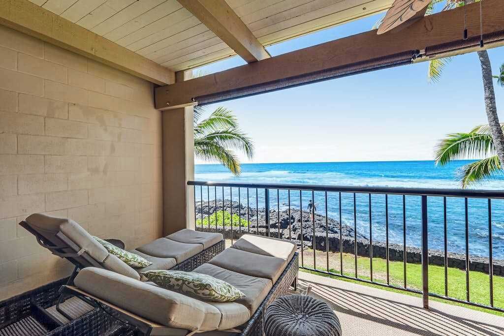 A balcony with a view of the ocean, a wicker sofa with cushions, and a small round table.
