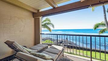 A balcony with a view of the ocean, a wicker sofa with cushions, and a small round table.