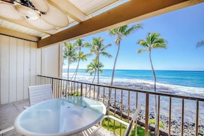 Ein Balkon mit einem Glastisch, einem weißen Stuhl und Blick auf Strand und Meer.