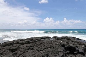 Une côte rocheuse où les vagues s’écrasent sur le rivage sous un ciel partiellement nuageux.