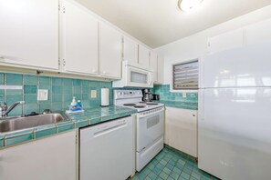 A compact kitchen with white cabinets, a microwave, a stove, and a refrigerator. - Oceanfront Kona Bali Kai 318 at Magic Sands Beach - Pool, Hot Tub, Laundry, WIFI (Kailua-Kona)