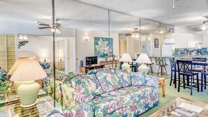 Una sala de estar con sofá, lámparas, una zona de comedor y una cocina al fondo.