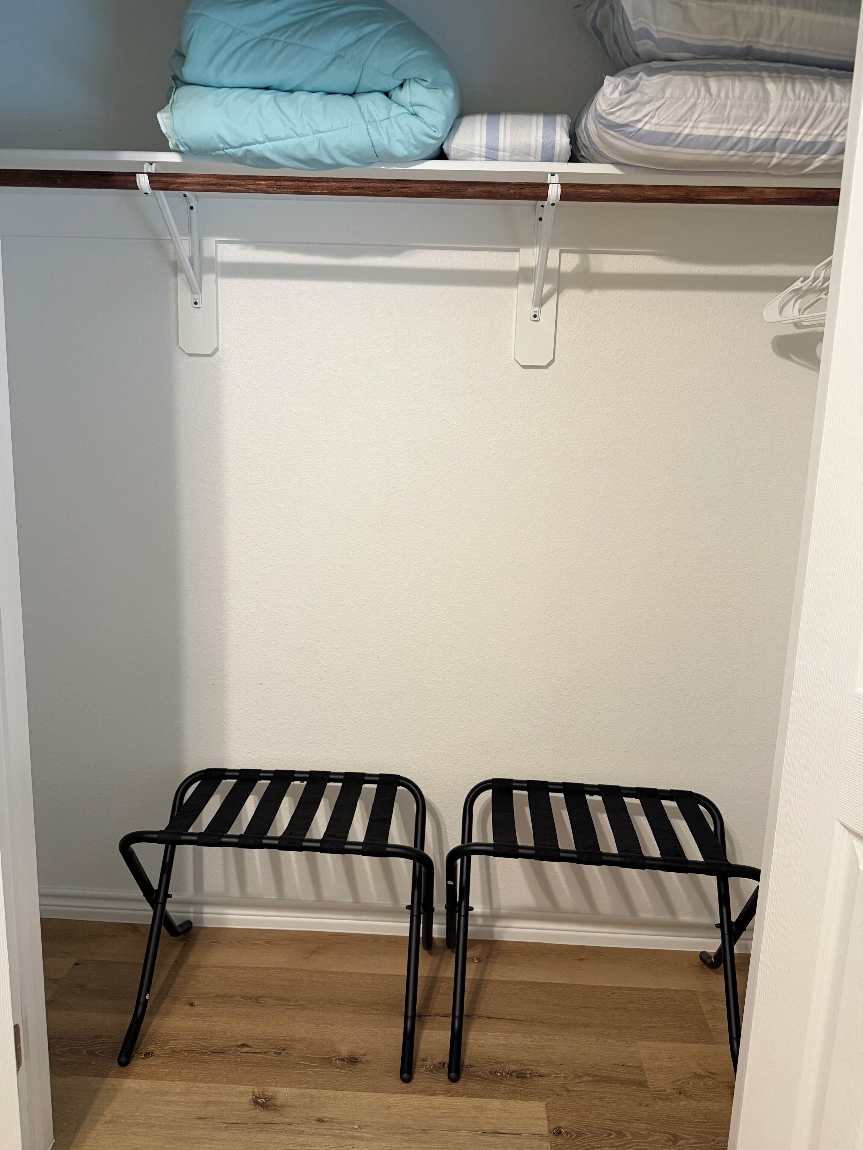 Ein Schrank mit Holzregal, Kleiderstange und zwei Metallstühlen.