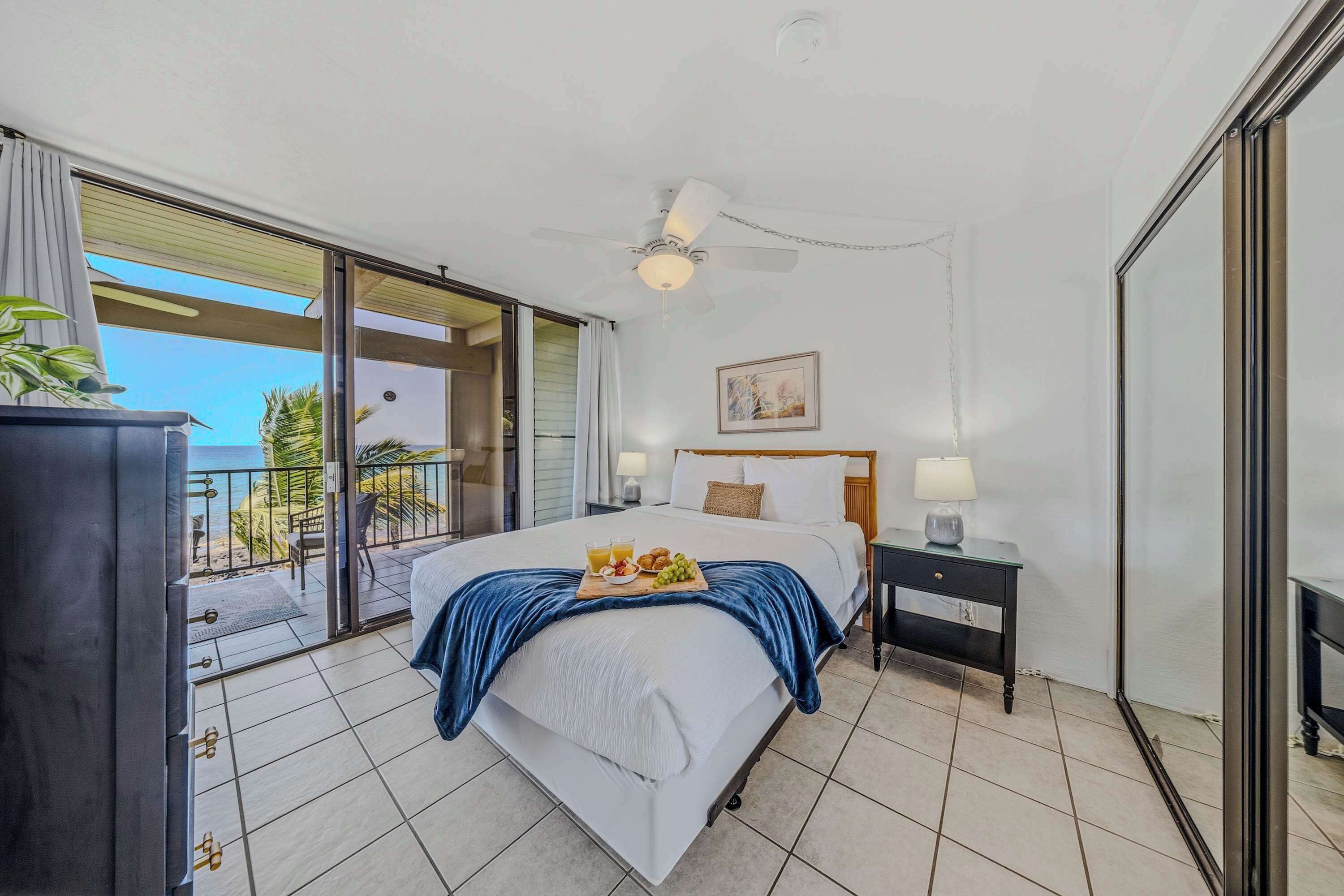 A hotel room with a bed, a nightstand, a ceiling fan, a window with a view, and a balcony.