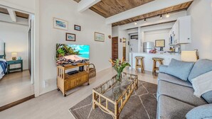Een woonkamer met een televisie, bank, salontafel en een keukenhoek met barstoelen.