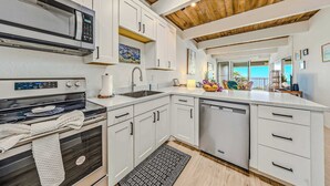 Een moderne keuken met witte kasten, een RVS magnetron, een inbouwoven en een vaatwasser.