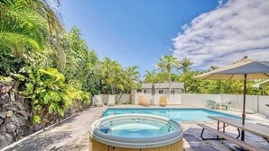 Un patio trasero con jacuzzi, piscina y zona de estar con sillas y una mesa.