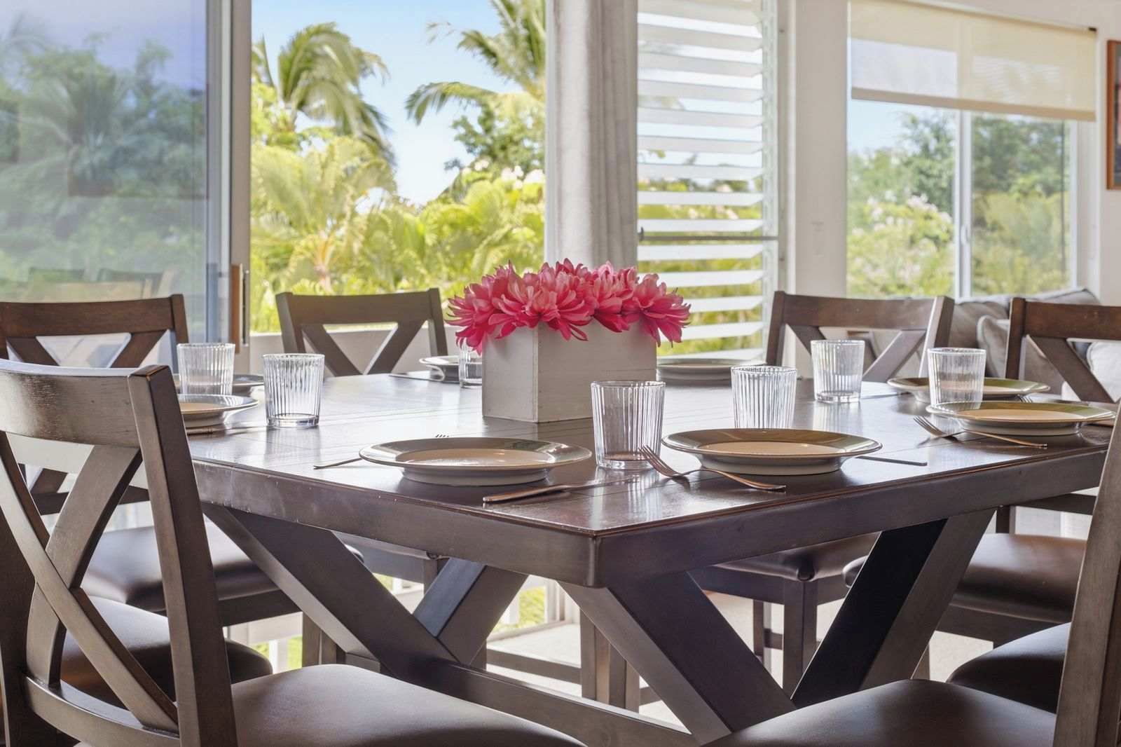 A dining table set for six with chairs, a vase of flowers, and clear glasses.