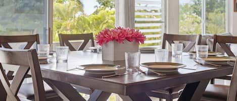 A dining table set for six with chairs, a vase of flowers, and clear glasses.